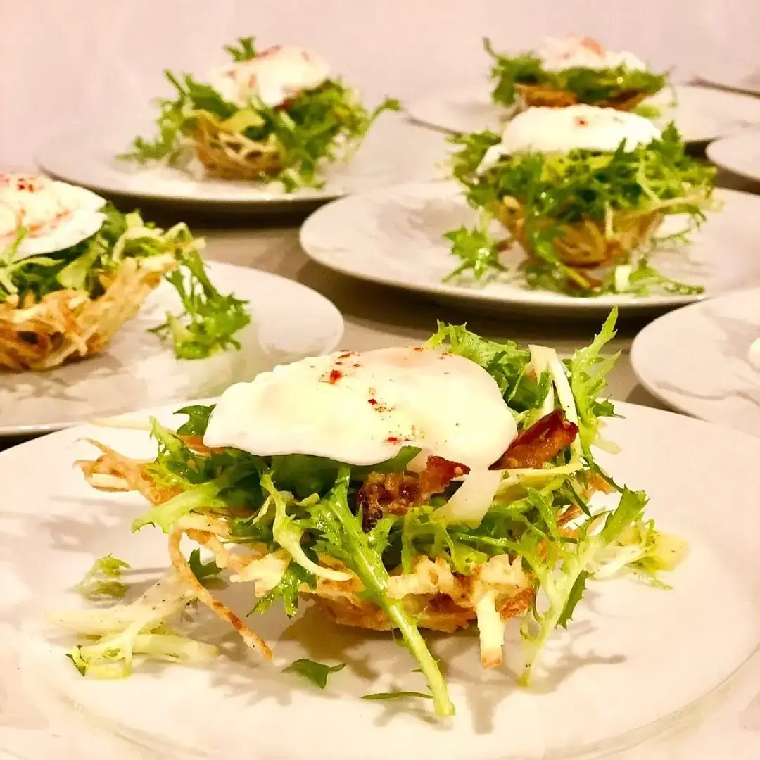Plated frisee salads served in crisp potato nests with a soft egg.