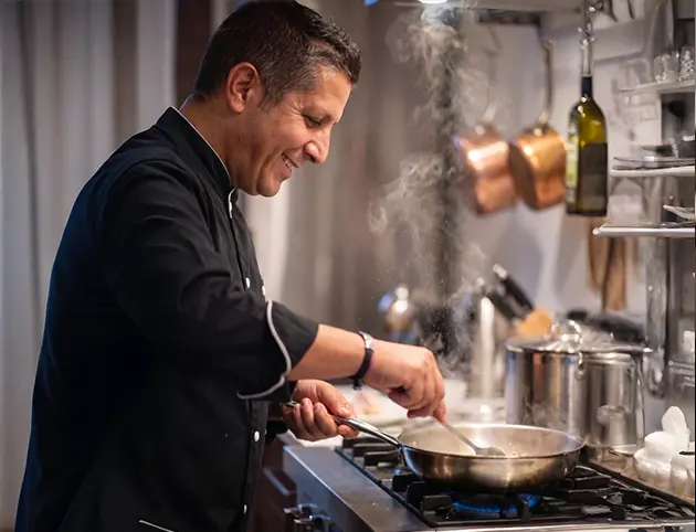 Chef cooking over a stove in a professional kitchen.