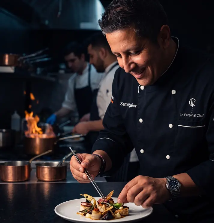 Chef plating a dish in a dark professional kitchen.