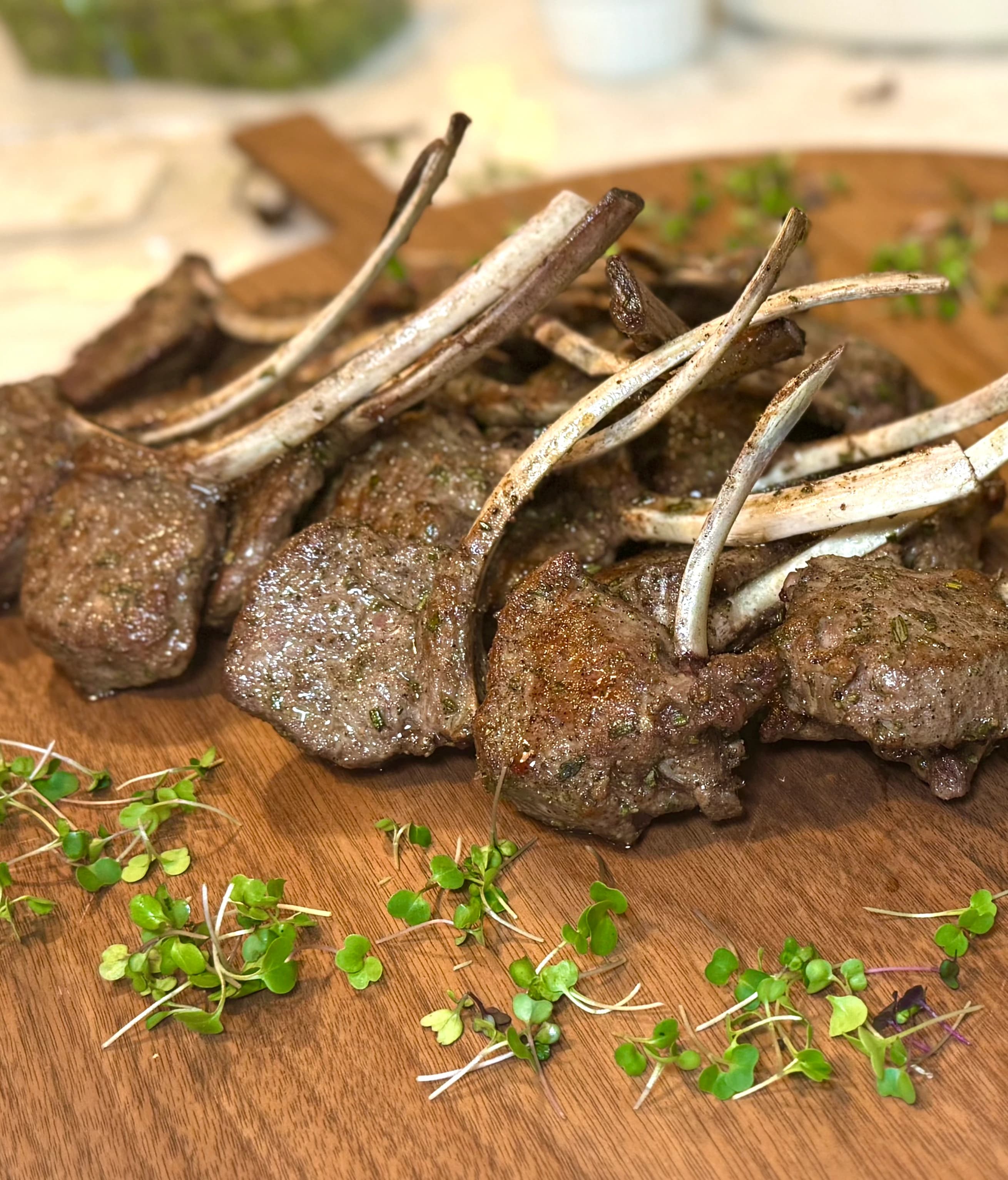 Charred herb lamb chops arranged on a wooden board with microgreens.